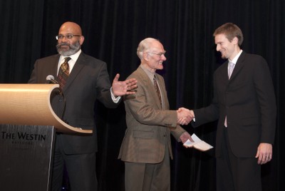Sam Abraham in foreground, with Dr. Lloyd Skarsgard and Ryan Morin shaking hands.